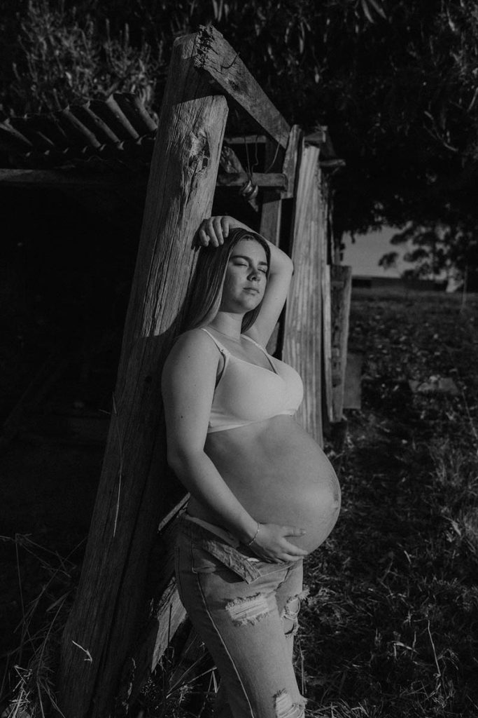 black and white image of a pregnant woman leaning on a barn with her eyes closed