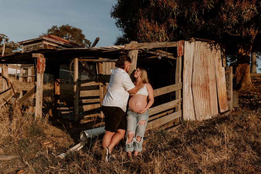 Young pregnant couple lining on a wooden barn looking at each other