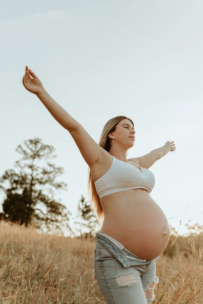young pregnant lady in a field a golden hour with her arms up