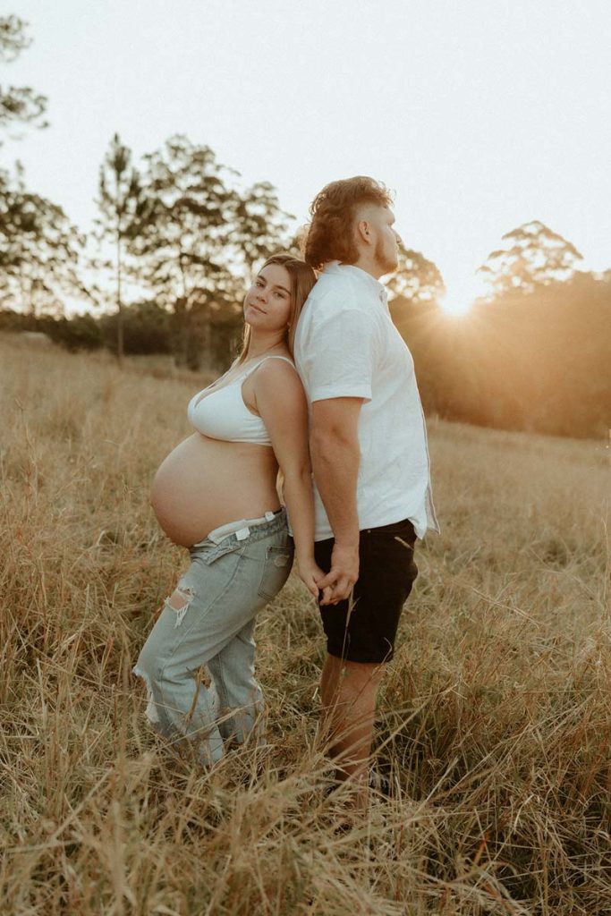 pregnant couple standing back to back in a field