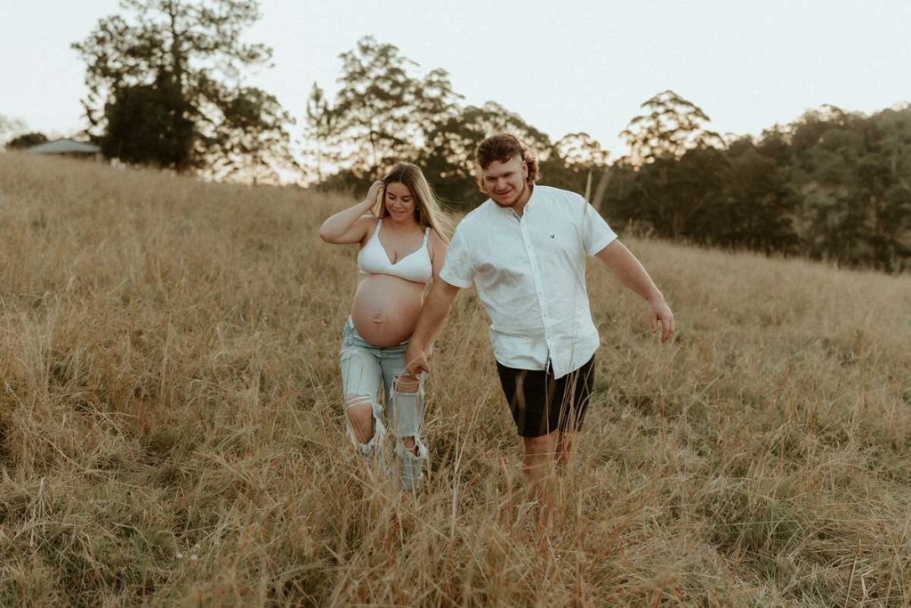 pregnant couple laughing walking in a field