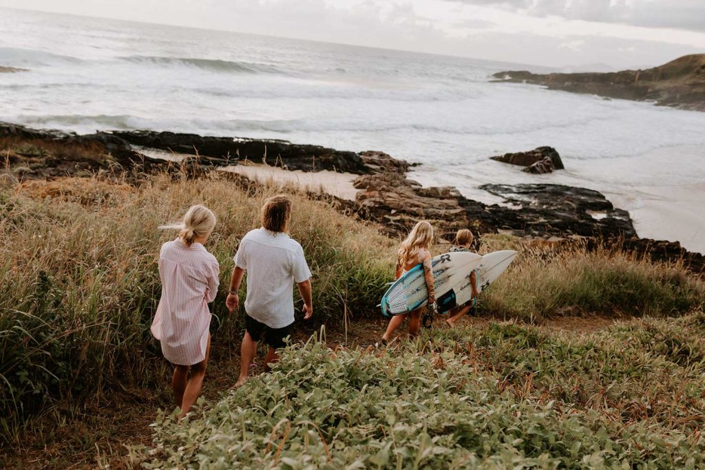 Family walking down the beach holding their surfboards