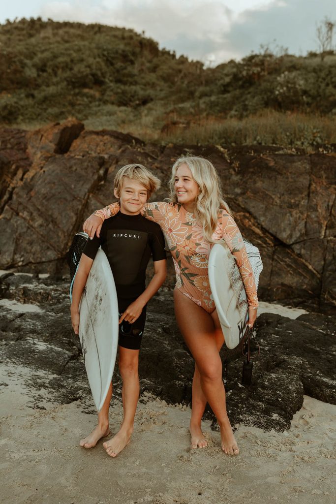 Brother and sister holding their surfboards and smiling