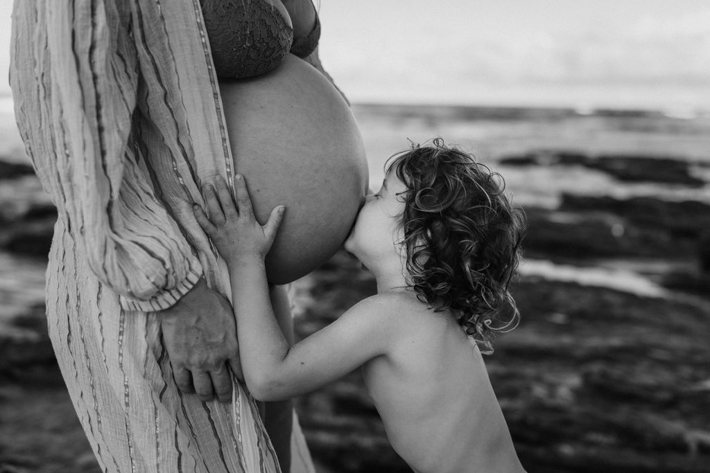 A young boy is kissing is mum's pregnant belly