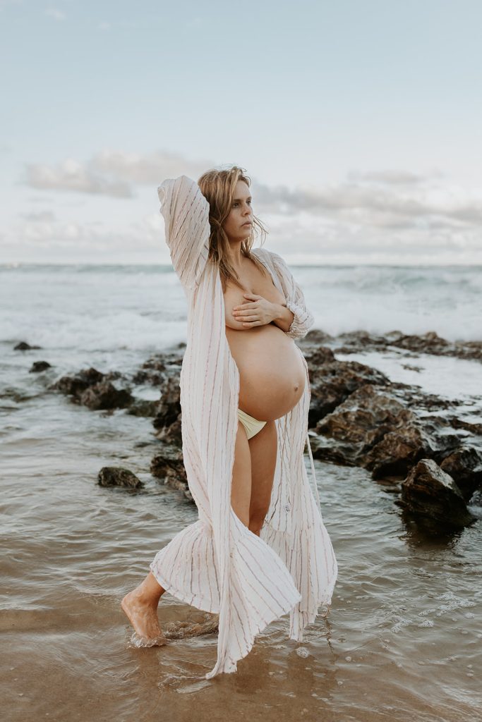 A beautiful pregnant woman standing in the ocean holding her breast with one hand